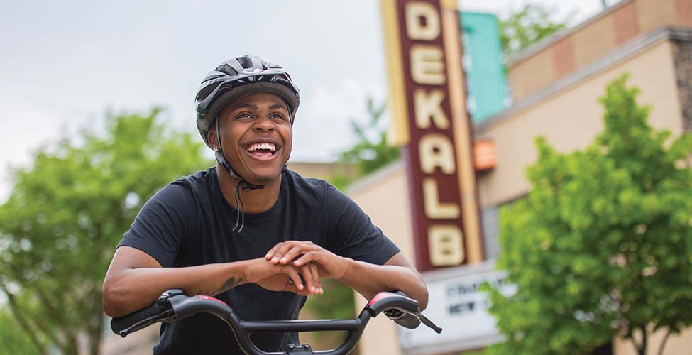 A person rides their bike in downtown DeKalb underneath a marquee sign that says "DeKalb."