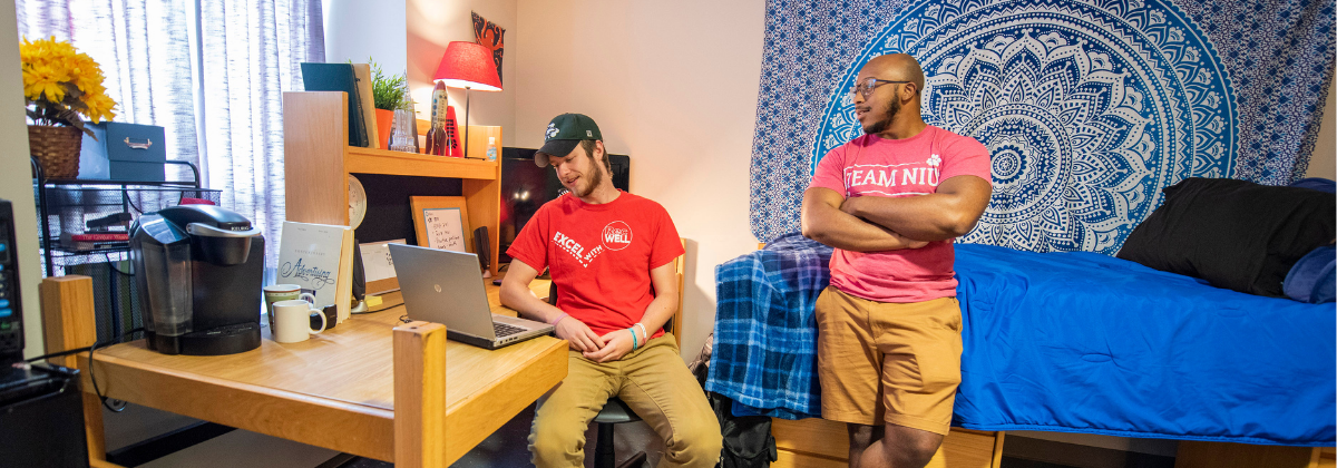 Two female residents talking in their room. One resident lies on a bed and the other is using a laptop.