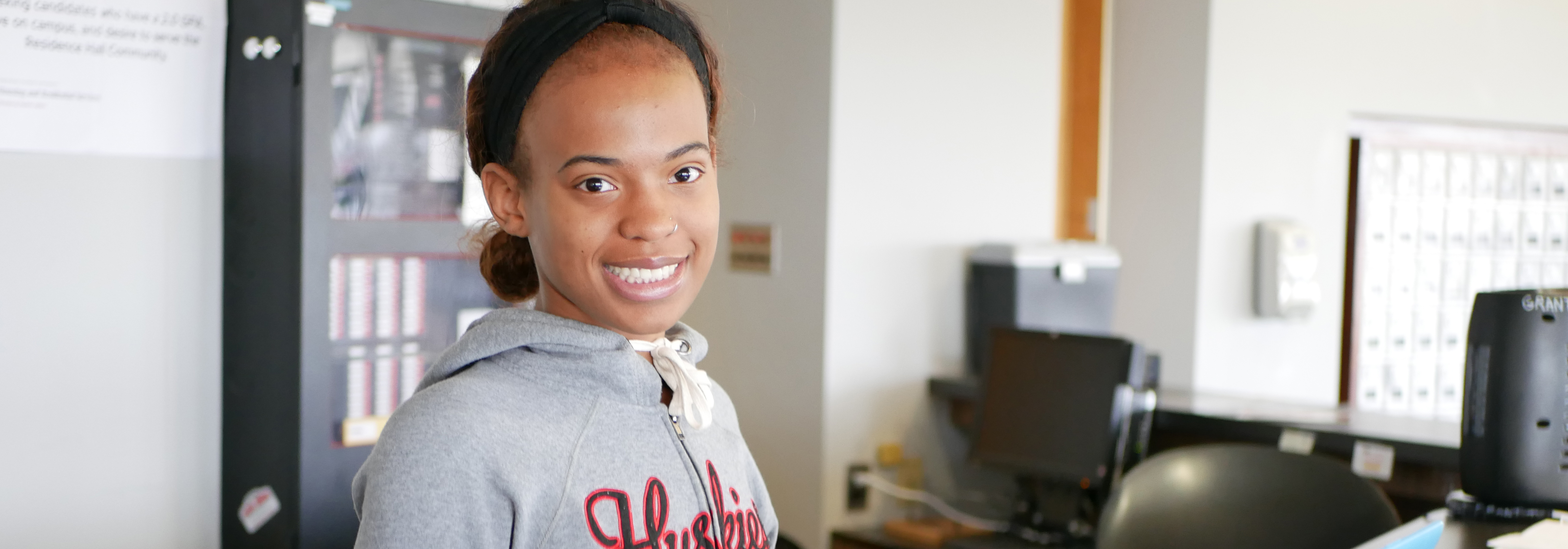 NIU student smiling behind desk.