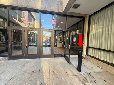 Accessible outer entrance to the School of Music between Boutell concert hall and the Music Library with an arrow pointing to the mechanical door opener