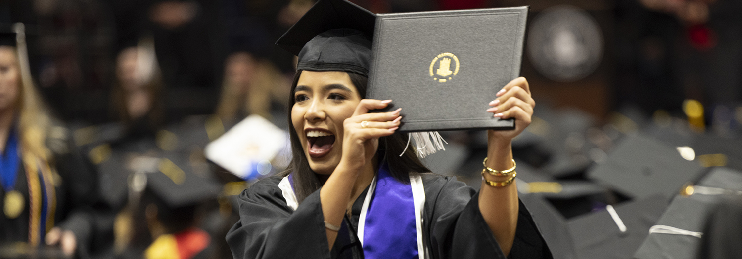 Student in graduation cap and gown holding up her degree at graduation