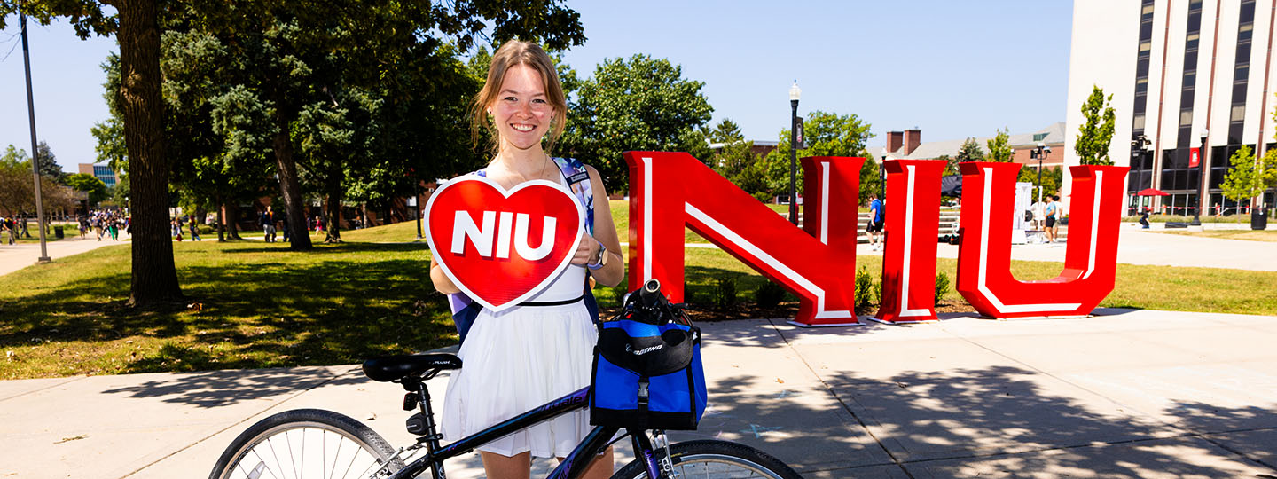 student poses in front of NIU sculpture