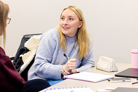 student holding pen and taking notes while discussing to colleague