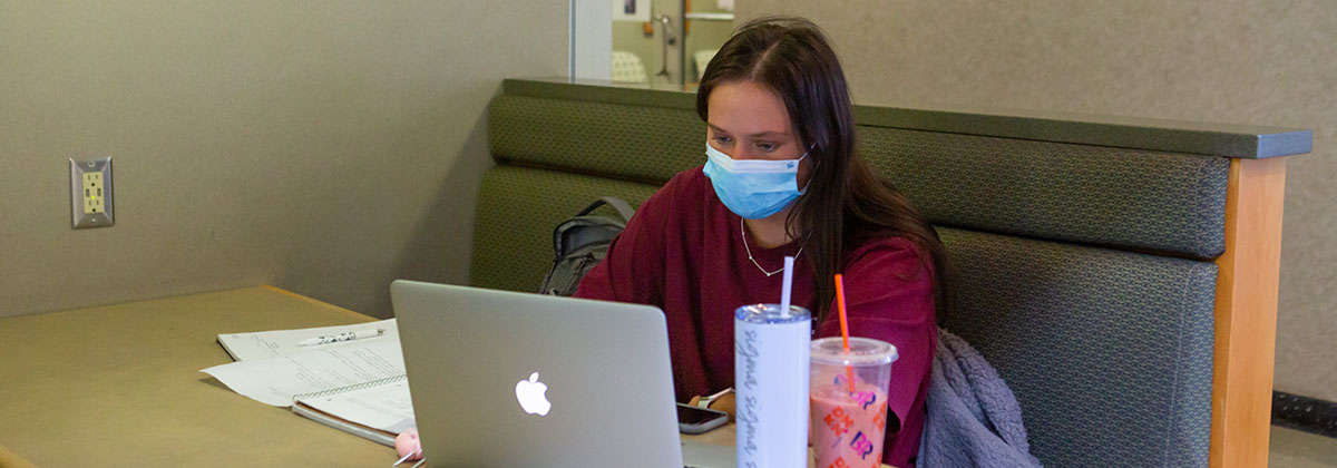 female student wearing mask working on laptop