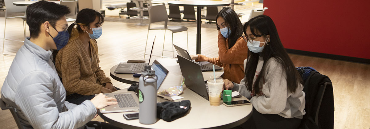 four students wearing masks, working on laptops