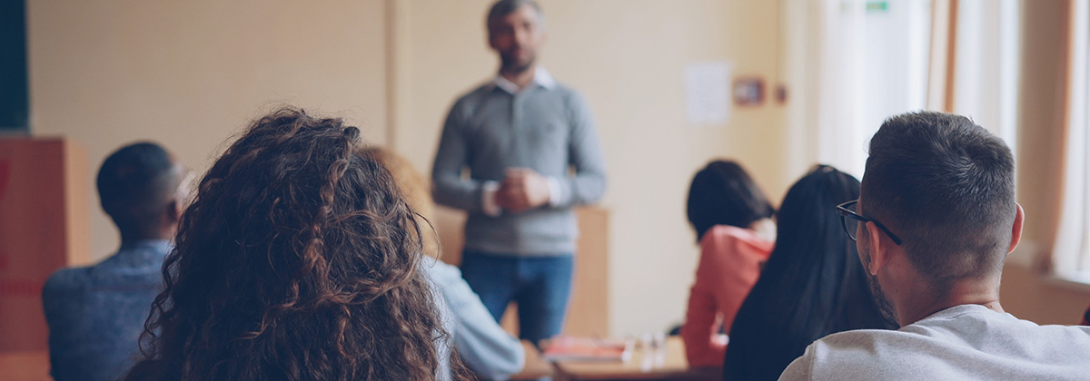 blurred image of male professor, viewed from the back of the classroom behind students
