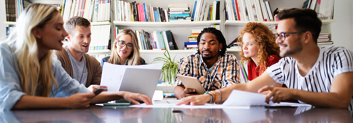 six people sitting at a table and working together with papers in the middle of the table