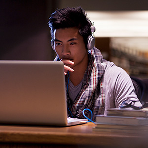 male student wearing headphones and looking at laptop screen