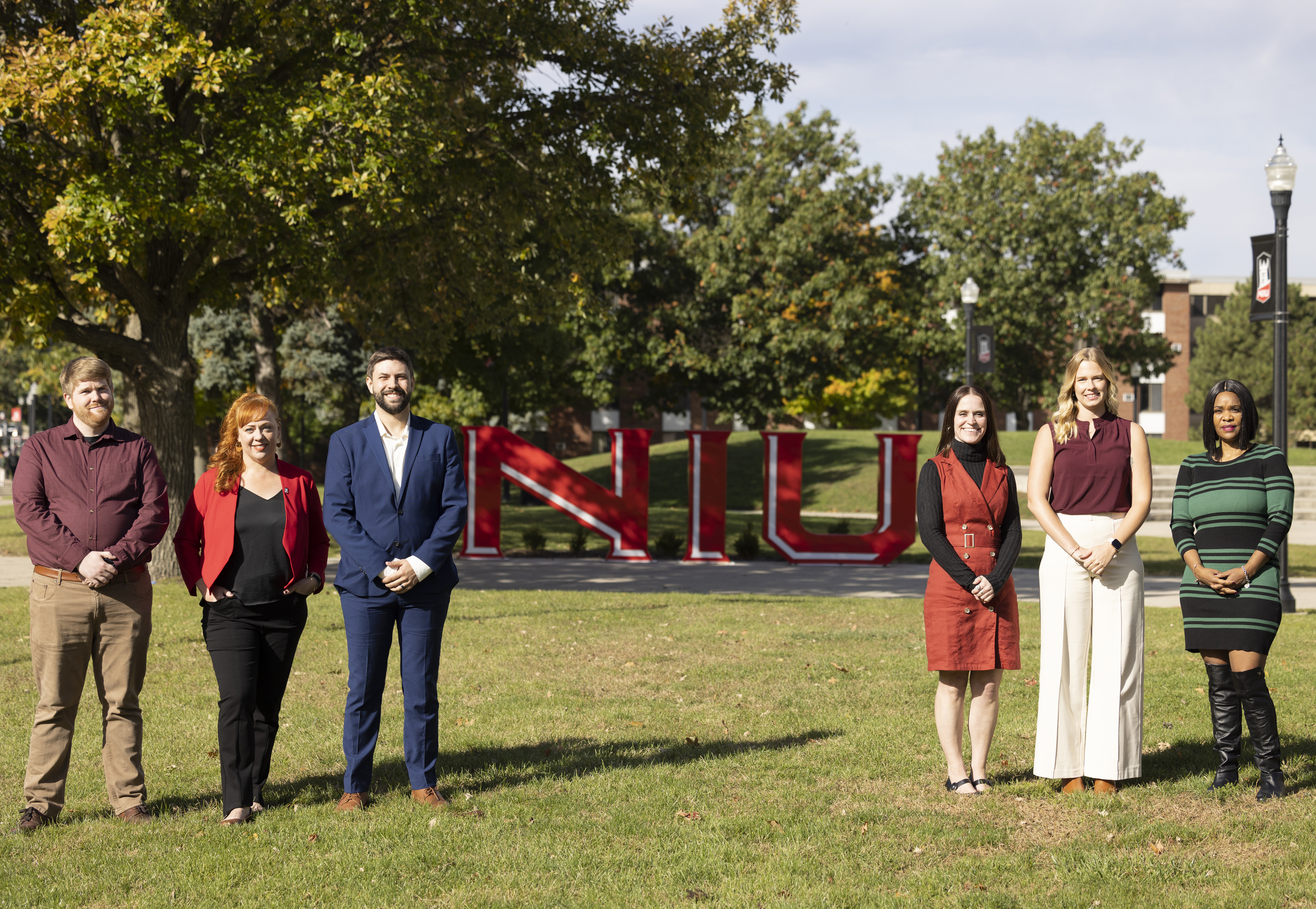 6 members of the Office of Online Learning stand on grass with the NIU letters visible in the distance