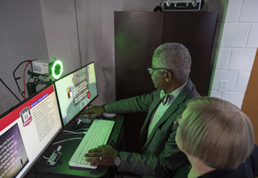 male faculty member using keyboard and button panel to configure a video recording studio with the assistance of a female member of CITL