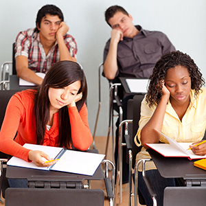 four students sitting at desks in a classroom with bored facial expressions and body language