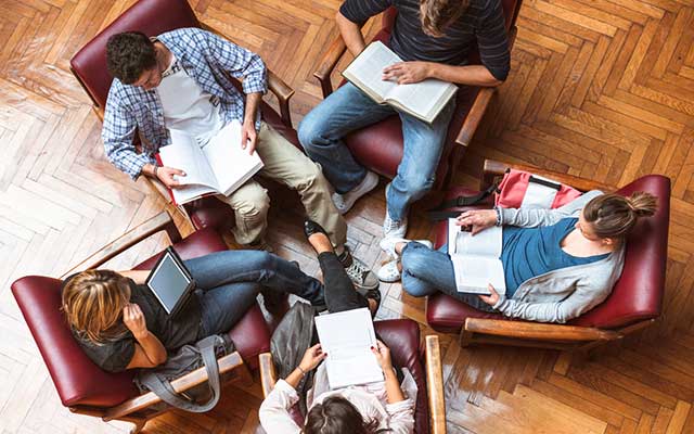 four students sitting in chairs reading