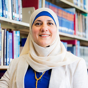 portrait of Rana Jaber standing in front of library shelves full of books