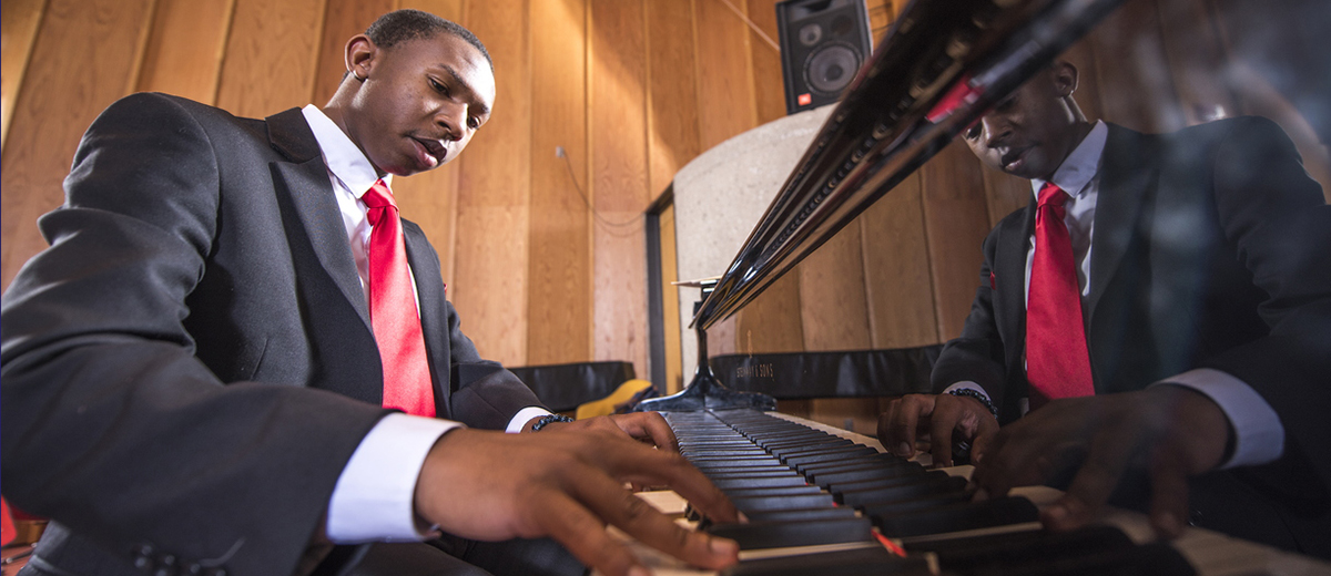 Male student in a suit performing at a piano.