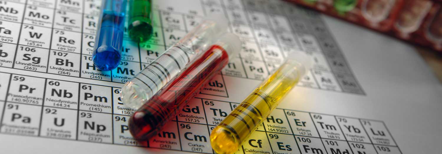 test tubes containing coloured solutions lying on top of printout of periodic table