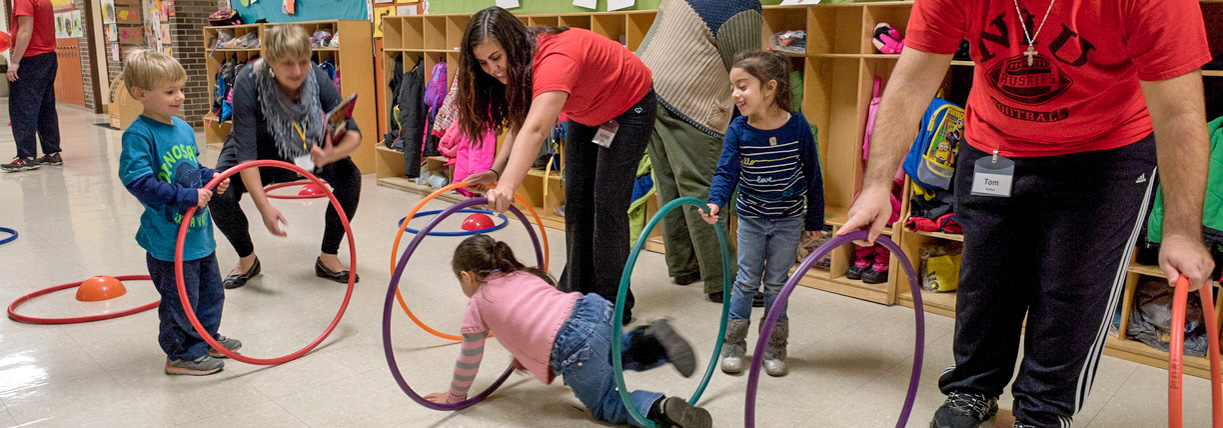 Student teacher aiding children crawling through hula hoops.