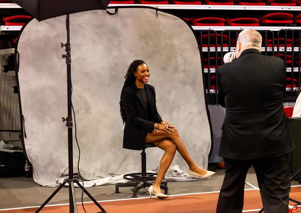 An NIU photographer photographs a seated subject in front of a portable backdrop at a career fair photobooth.