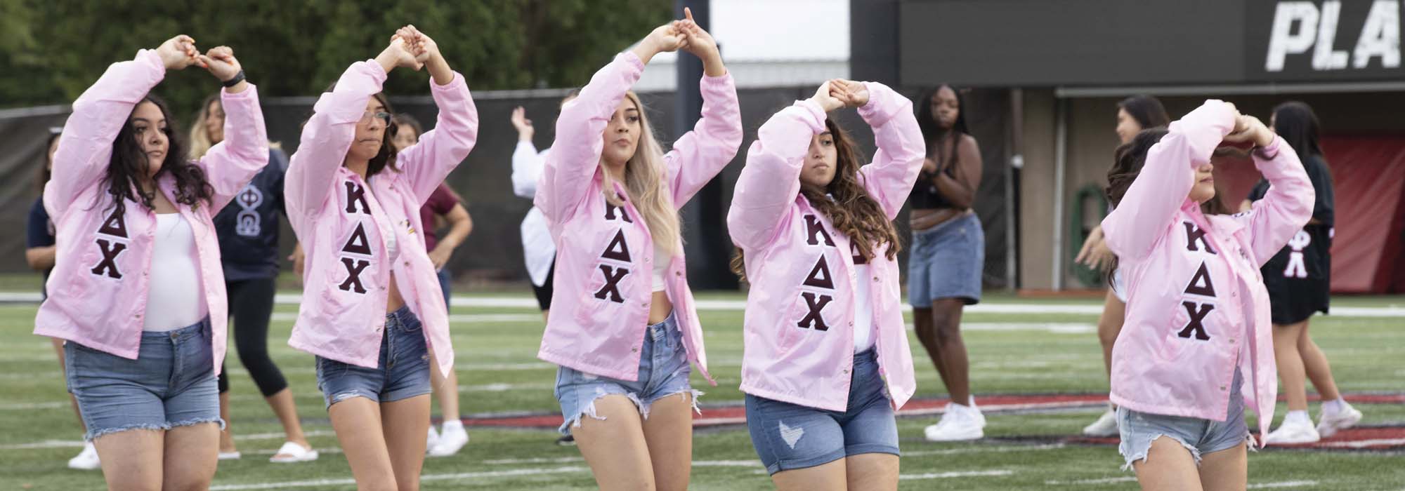 Members of Kappa Delta Chi perform at Huskie Stadium wearing matching pink jackets and denim shorts