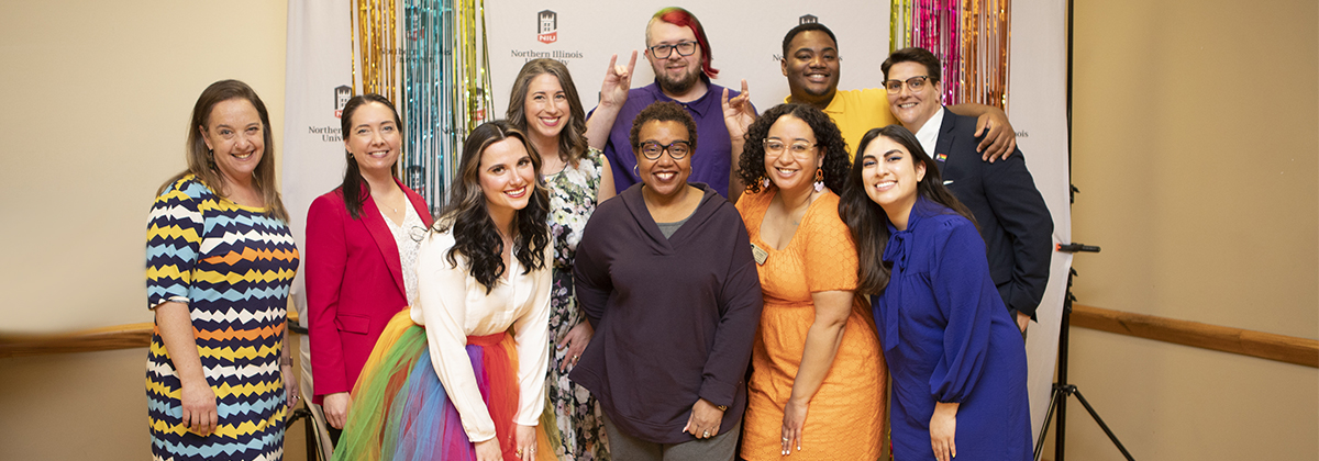 Group photo taken at the 2022 Pride Awards Ceremony. GSRC staff and faculty are seen in the photo wearing colorful attire and smiling in front of a NIU backdrop