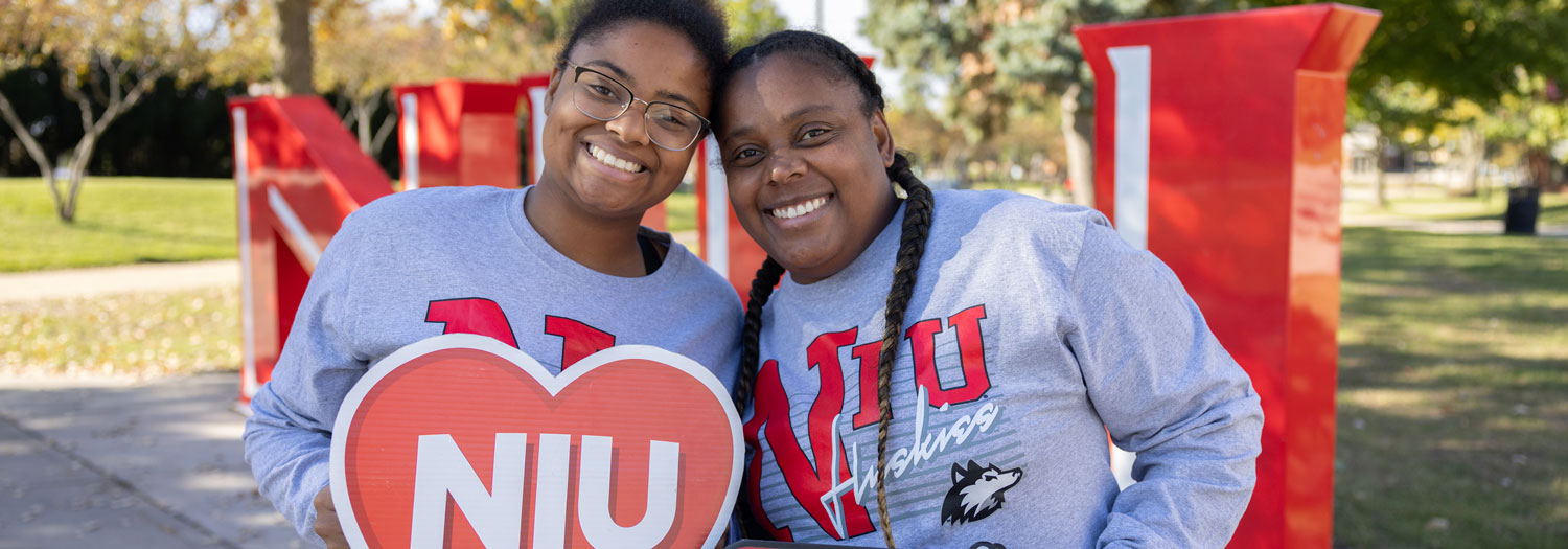 Happy parent and student at family weekend hold NIU sign