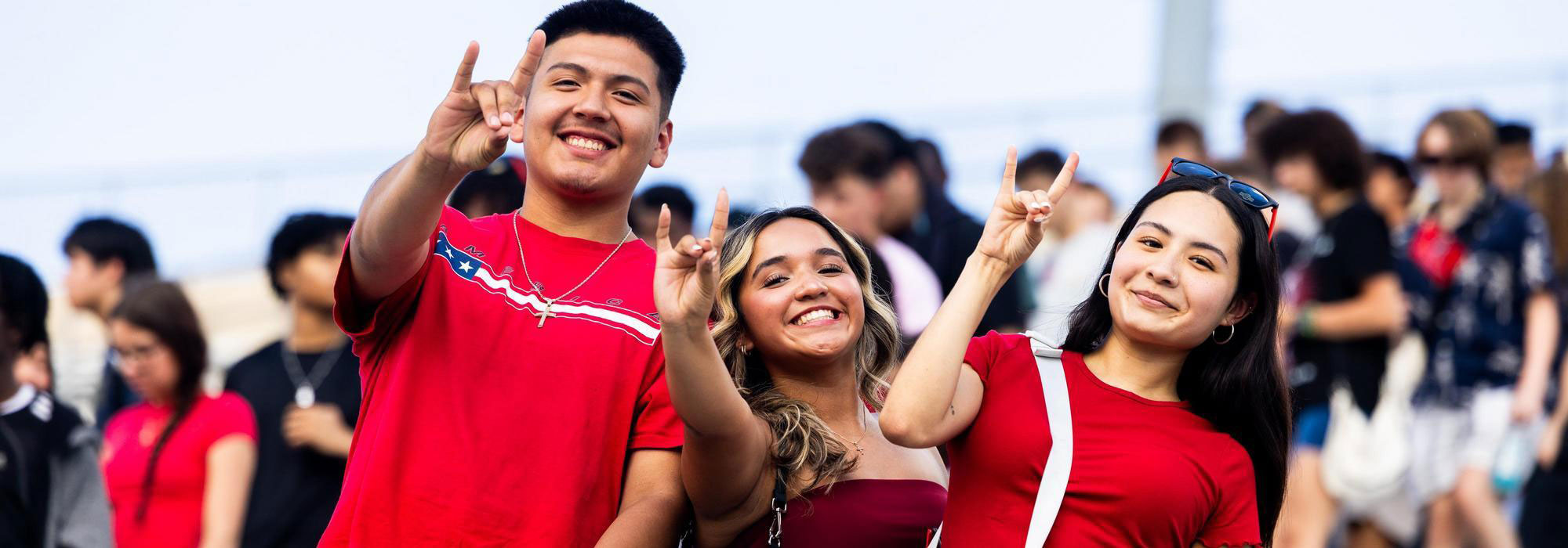 Three NIU students smiling and making the Huskie hand sign at an outdoor campus event
