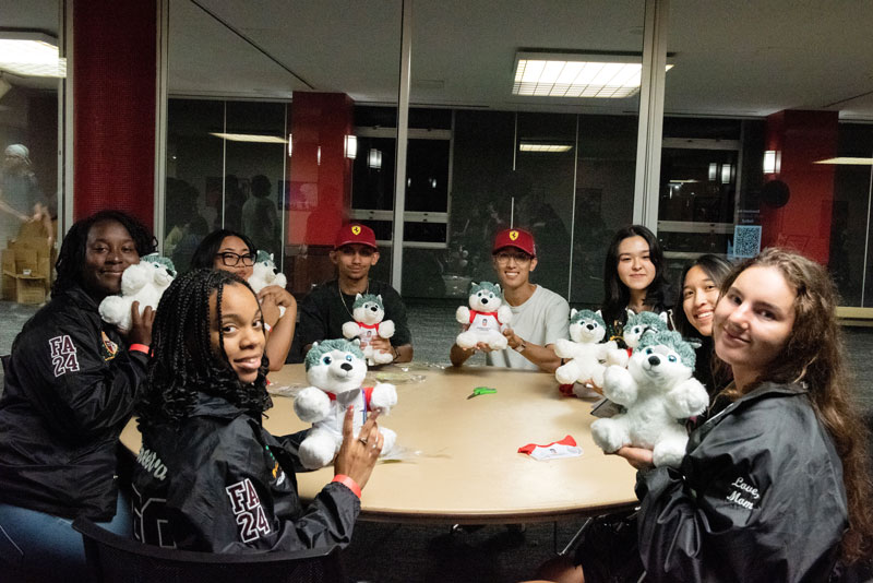 Students seated around a table holding stuffed Huskie mascots at a welcome event