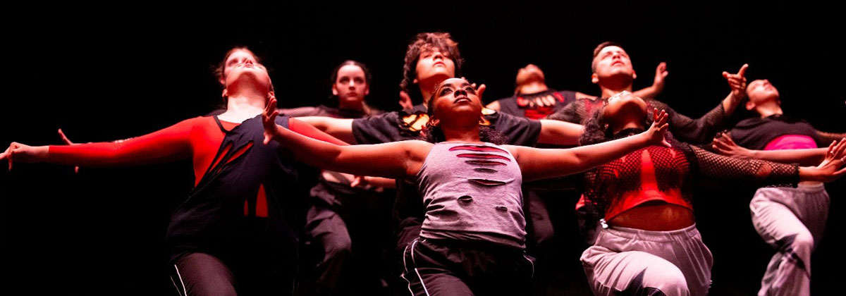Dancer in group on a dak stage under overhead lighting.